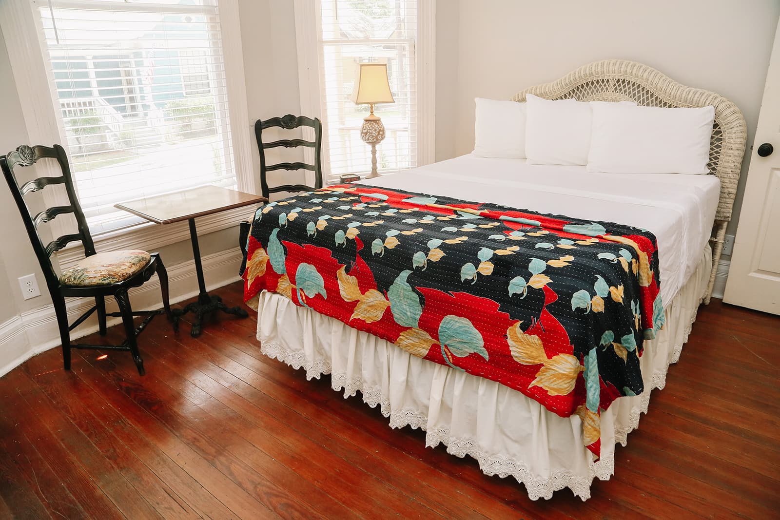 A cozy bedroom featuring a bed with a colorful quilt, a bedside lamp, and a small table with two chairs.