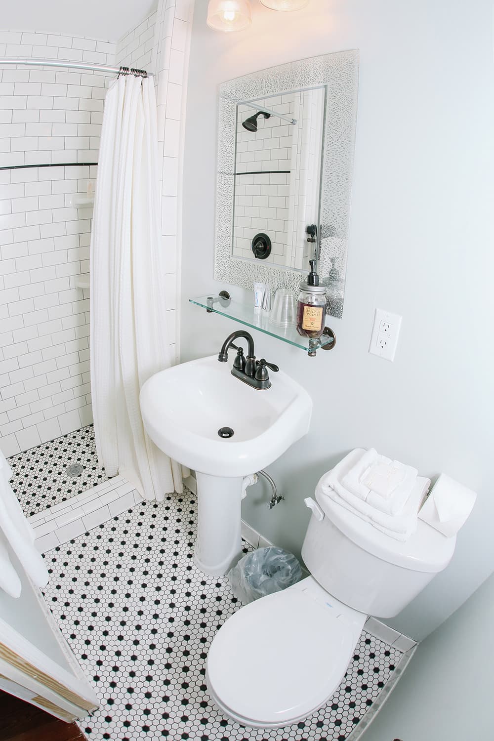 A small, modern bathroom featuring a walk-in shower, pedestal sink, toilet, and decorative black and white tiled floor.