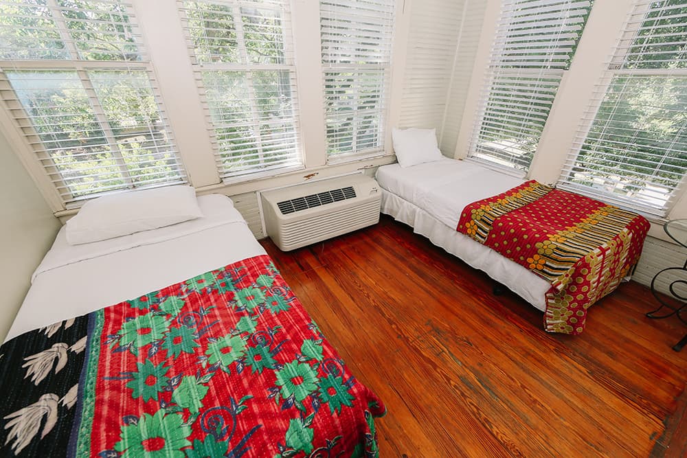 A cozy room featuring two twin beds with colorful blankets and large windows.