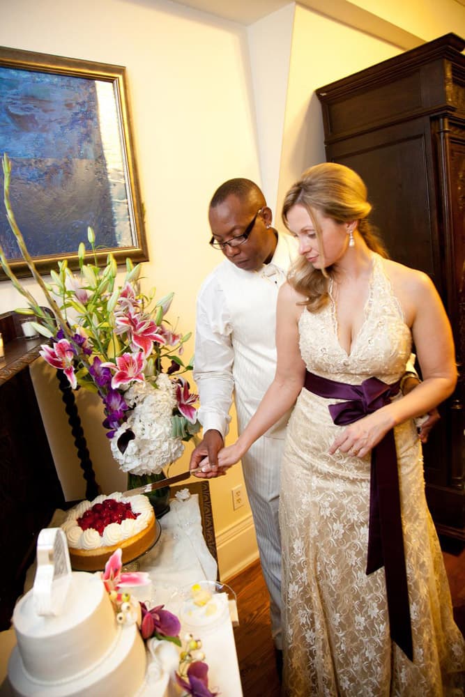 A couple in elegant attire cuts a cake together, surrounded by decorative flowers.