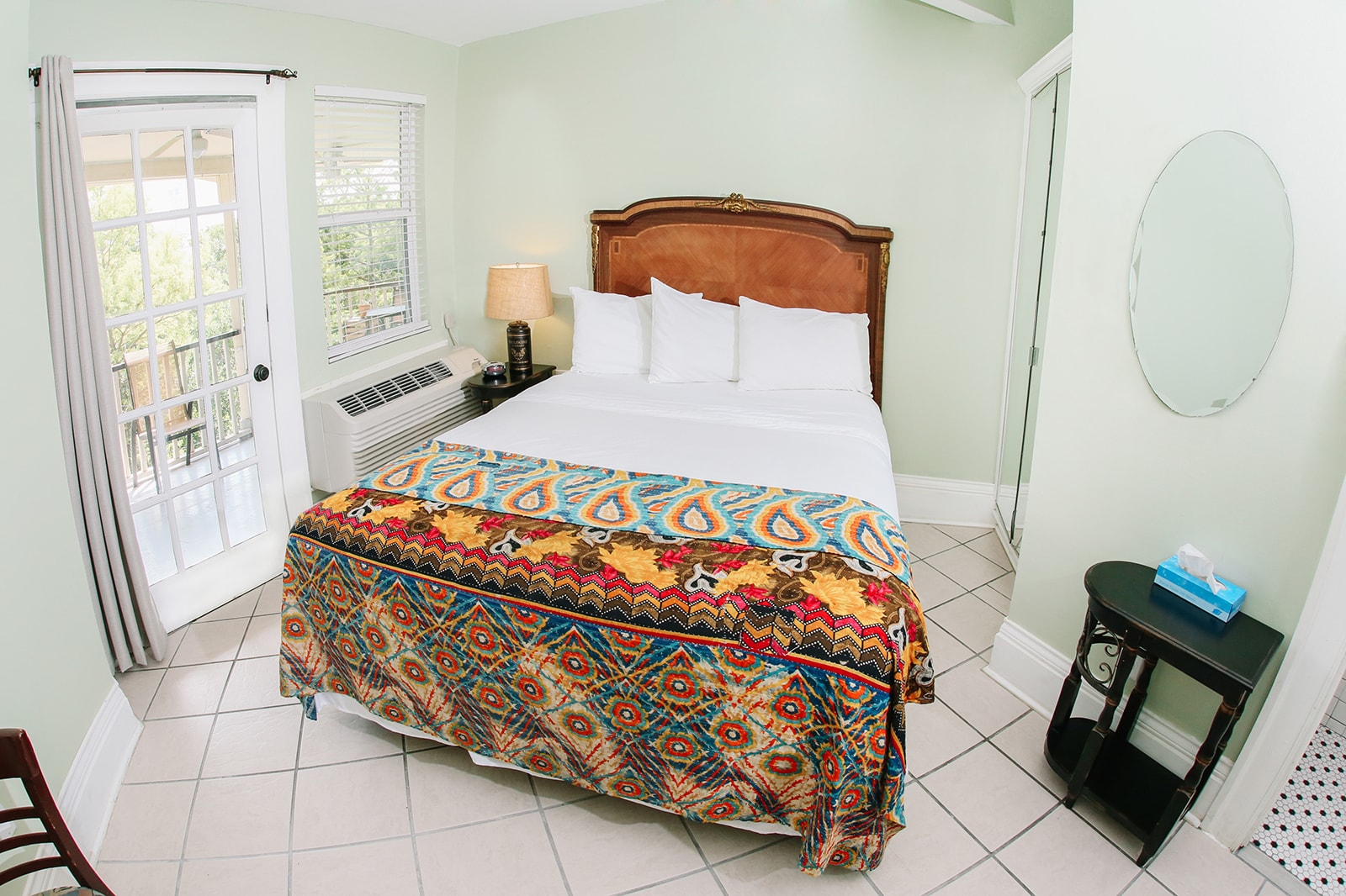 A cozy bedroom featuring a double bed with a colorful patterned throw, a nightstand, and a window with access to a balcony.