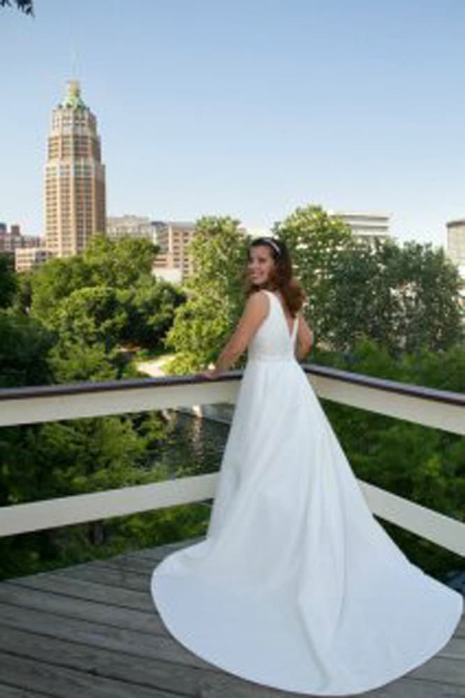 A woman in a white wedding dress stands on a balcony overlooking a city skyline.