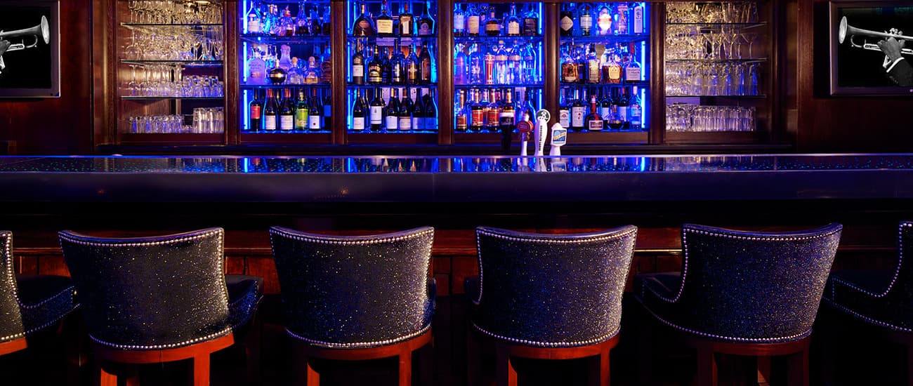 A stylish bar with illuminated shelves of liquor and velvet-upholstered stools.