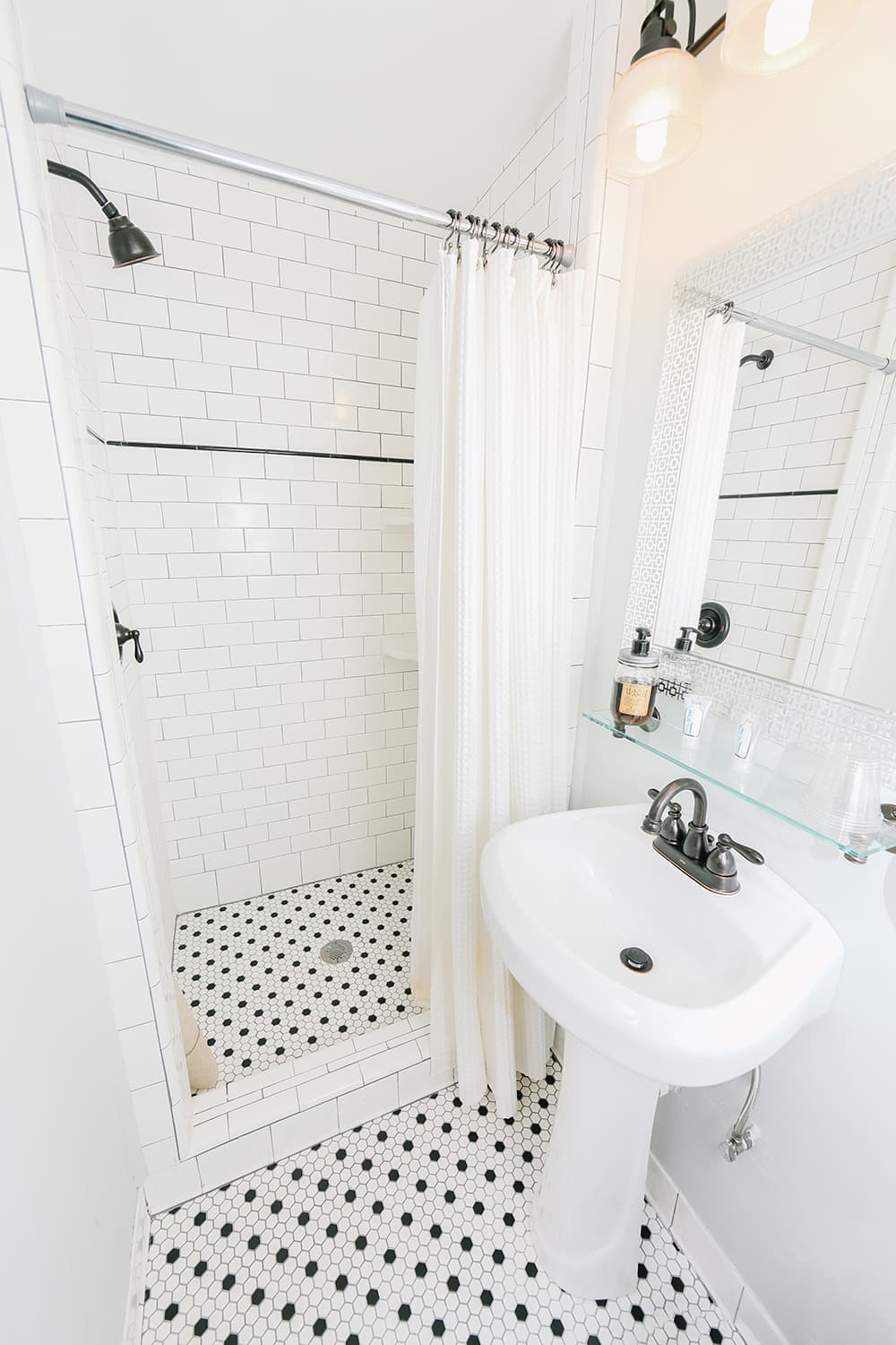 A modern bathroom featuring a walk-in shower with white tiles and a black-and-white hexagonal floor.