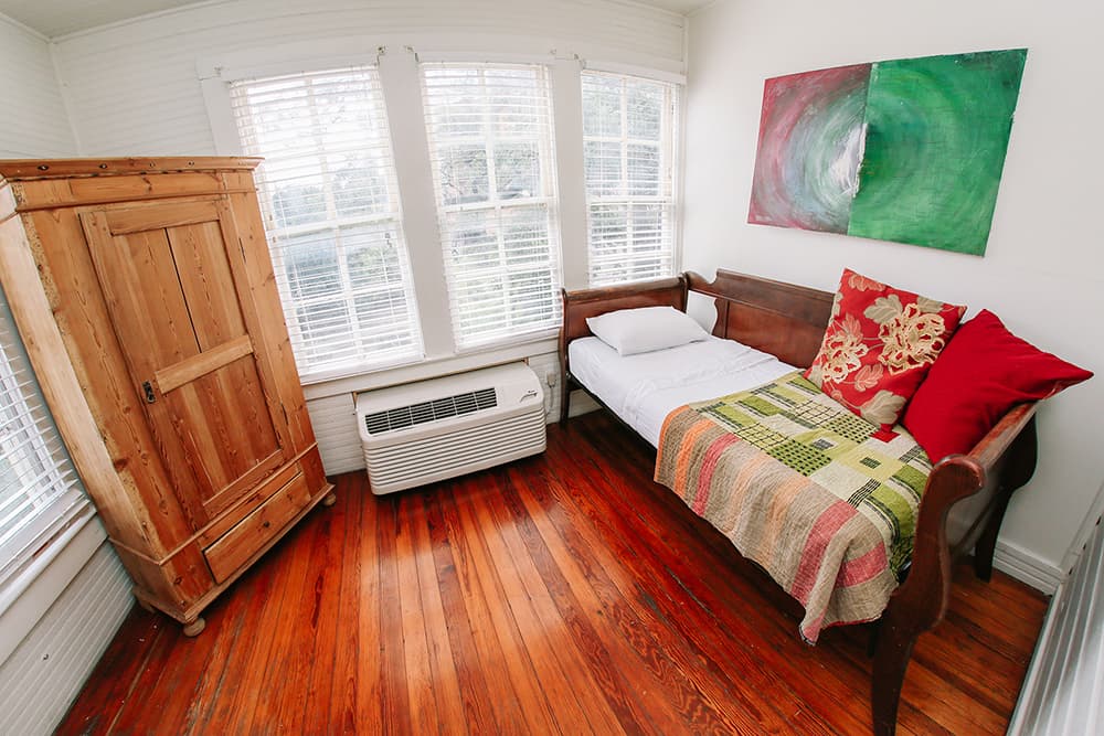Cozy room featuring a wooden armoire, a daybed with colorful pillows, and large windows letting in natural light.
