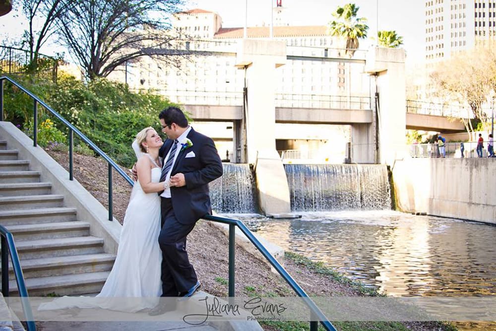 A joyful couple poses together on a staircase beside a flowing river and waterfall.