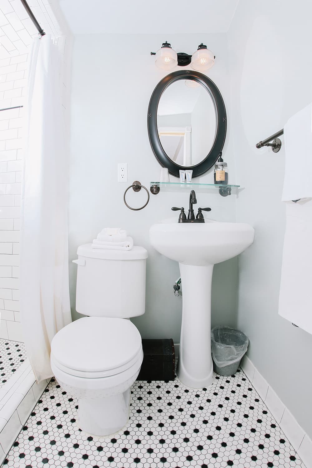A modern bathroom featuring a pedestal sink, a toilet, a round mirror, and hexagonal tile flooring.