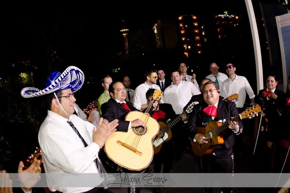 A lively mariachi band performs outdoors, surrounded by an engaged audience in a festive atmosphere.