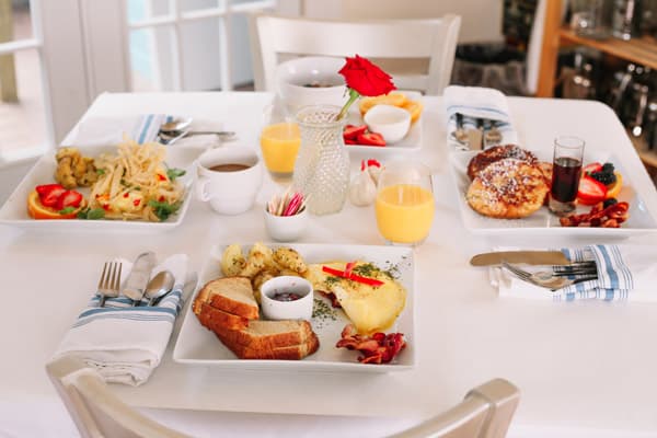 A beautifully arranged breakfast table featuring various dishes, including fruit, pastries, and eggs, with a flower centerpiece.