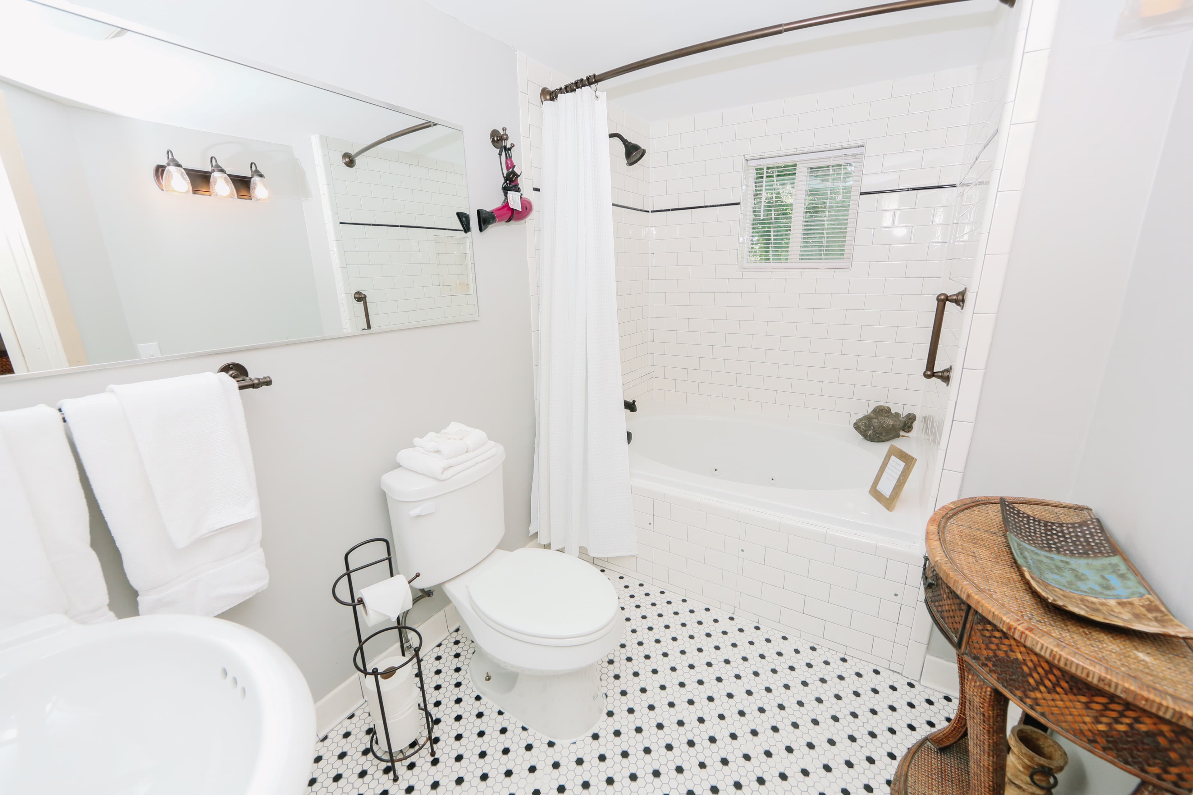 A bright bathroom featuring a white tub, sink, and black-and-white tiled floor.