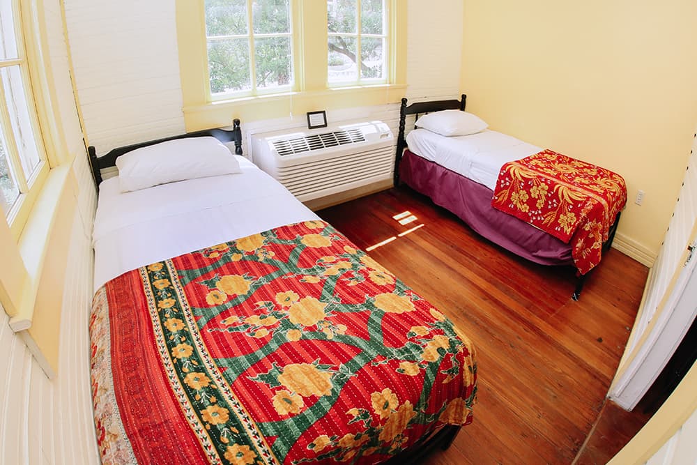 A cozy bedroom featuring two beds with colorful blankets and large windows.