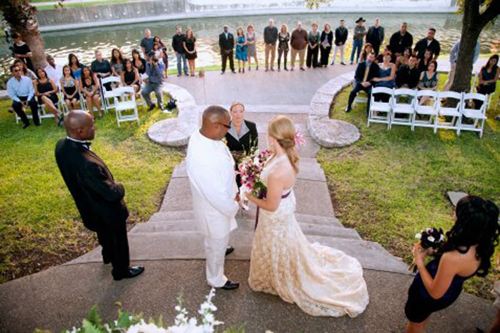 A couple exchanges vows during an outdoor wedding ceremony, surrounded by family and friends.
