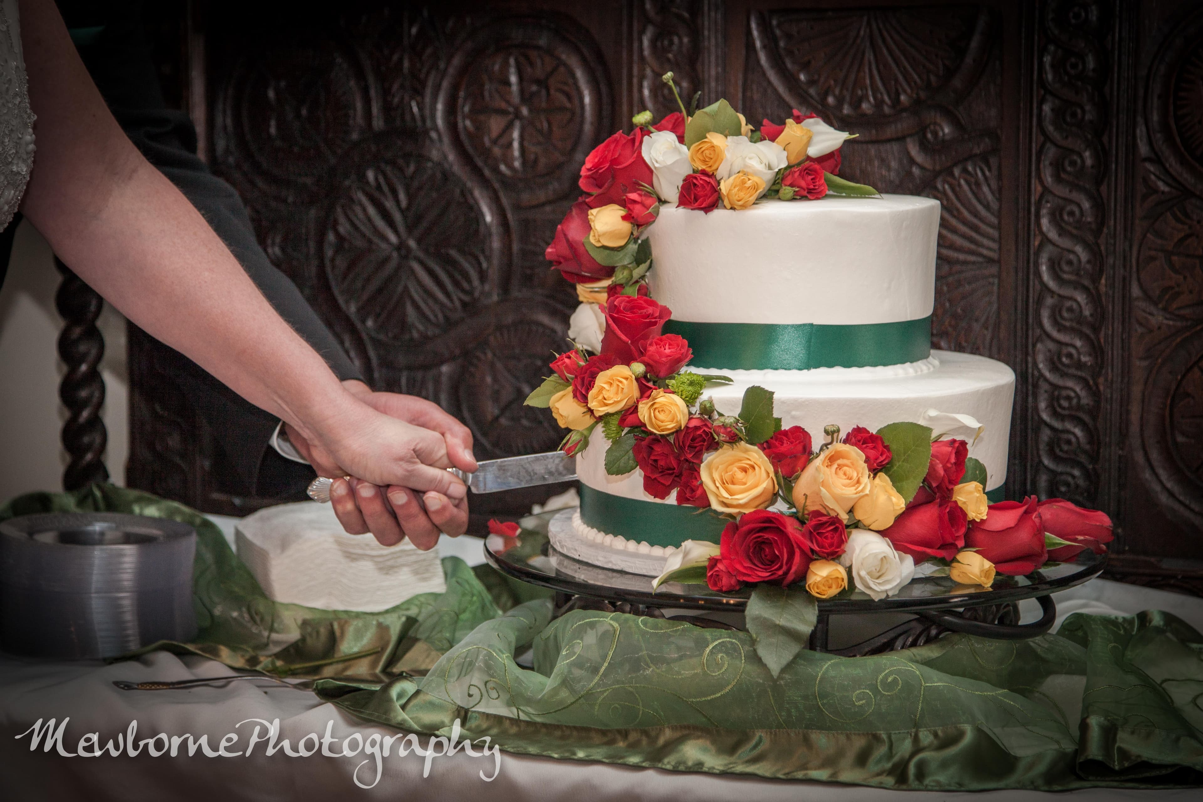 A hand holds a knife to slice a wedding cake adorned with vibrant flowers.