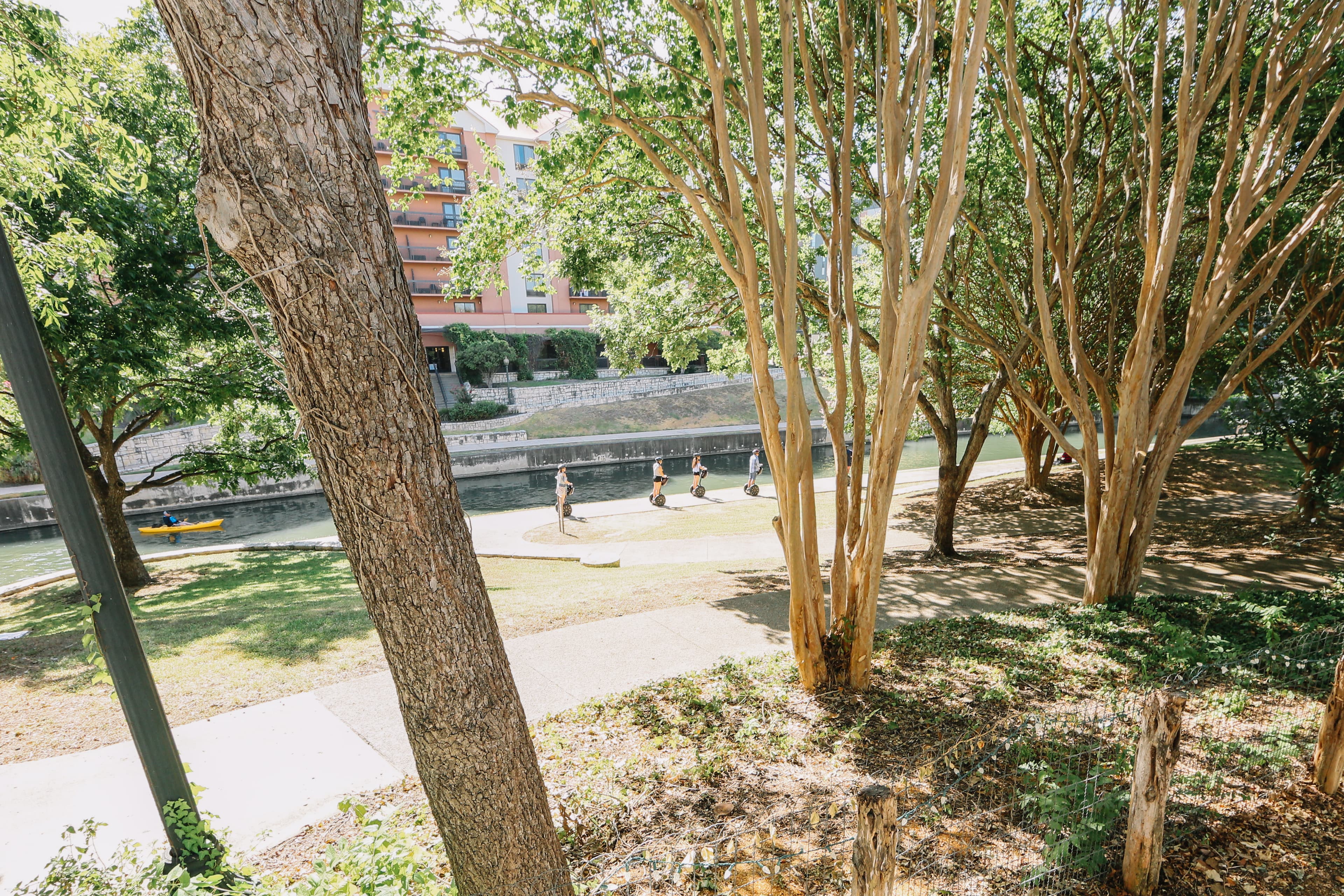 A view of a canal pathway bordered by trees, with people walking in the background.