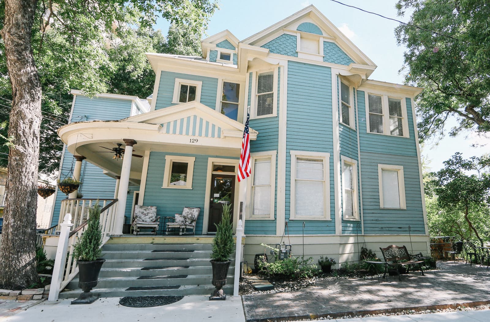 A charming blue Victorian-style house with a front porch and an American flag.