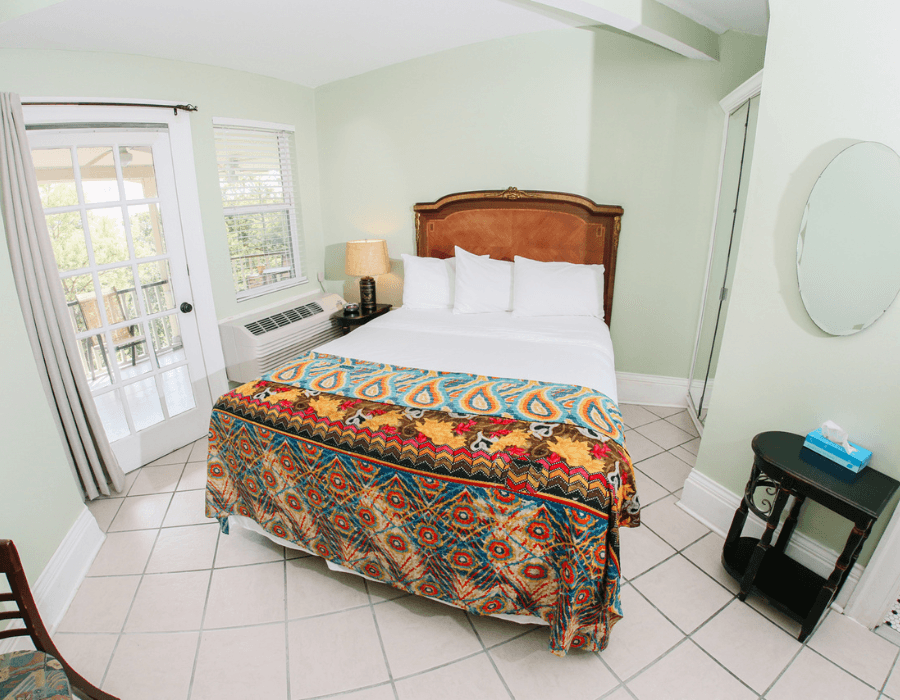 Brightly colored bedroom featuring a queen bed with a decorative blanket, chair, and access to a balcony.