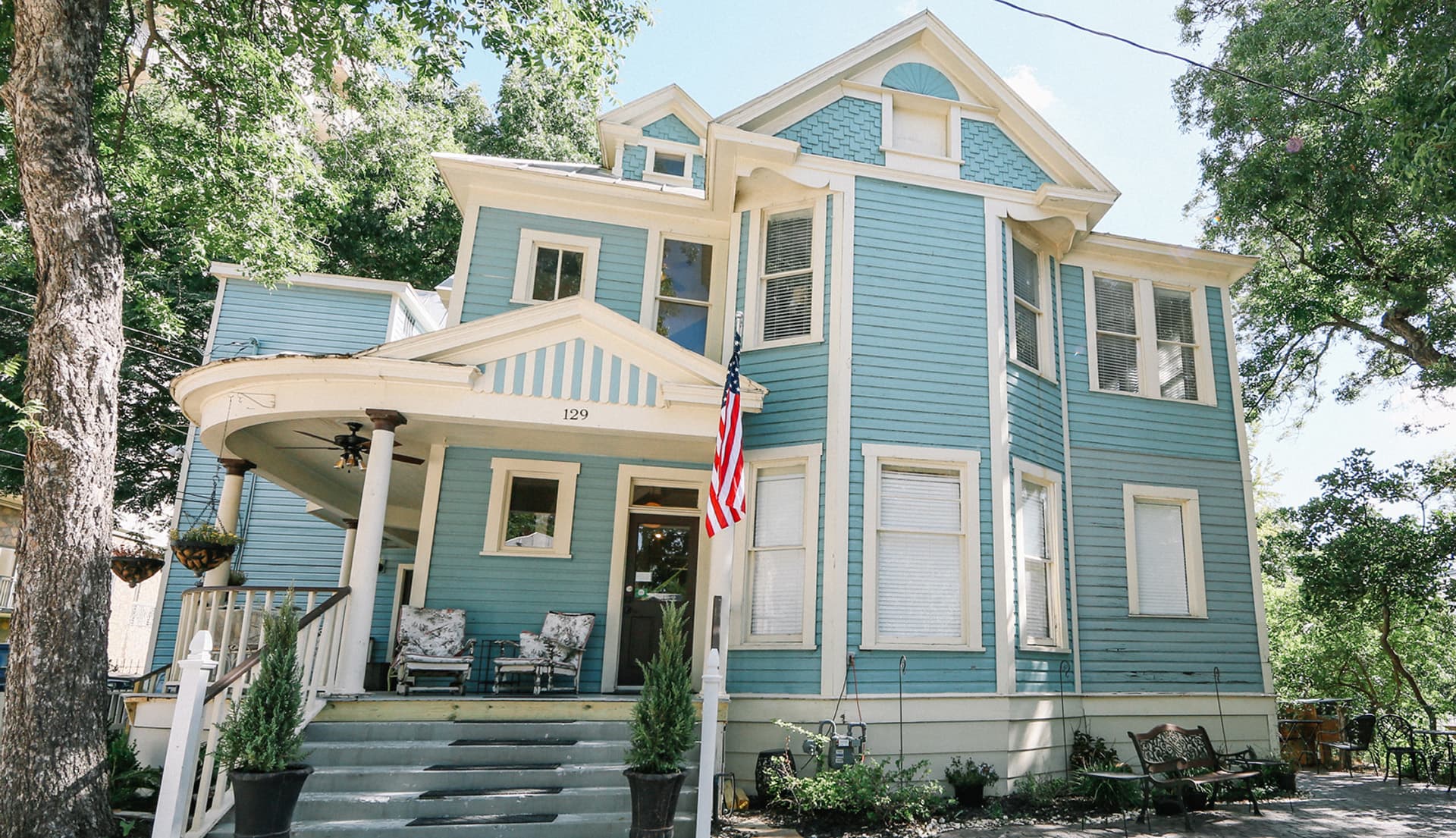 A large, two-story blue house featuring a front porch and American flag.