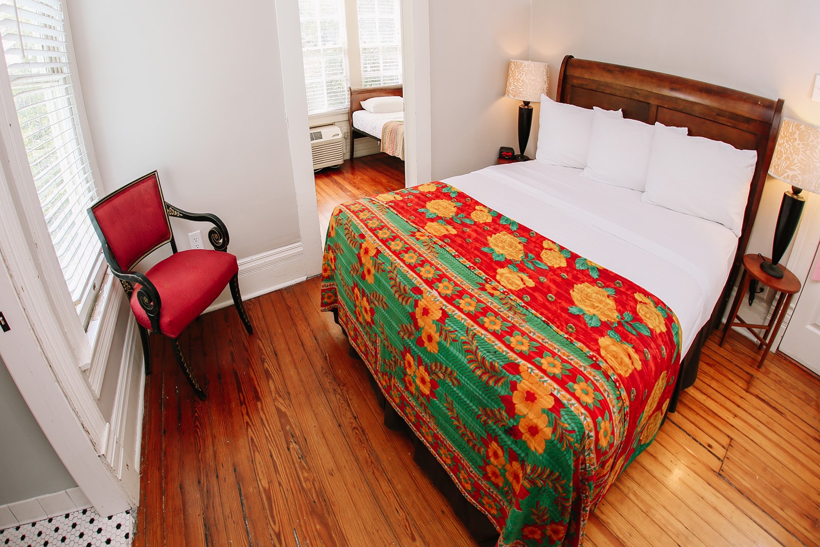 A cozy bedroom featuring a double bed with bright floral bedding, a wooden floor, and a red chair.