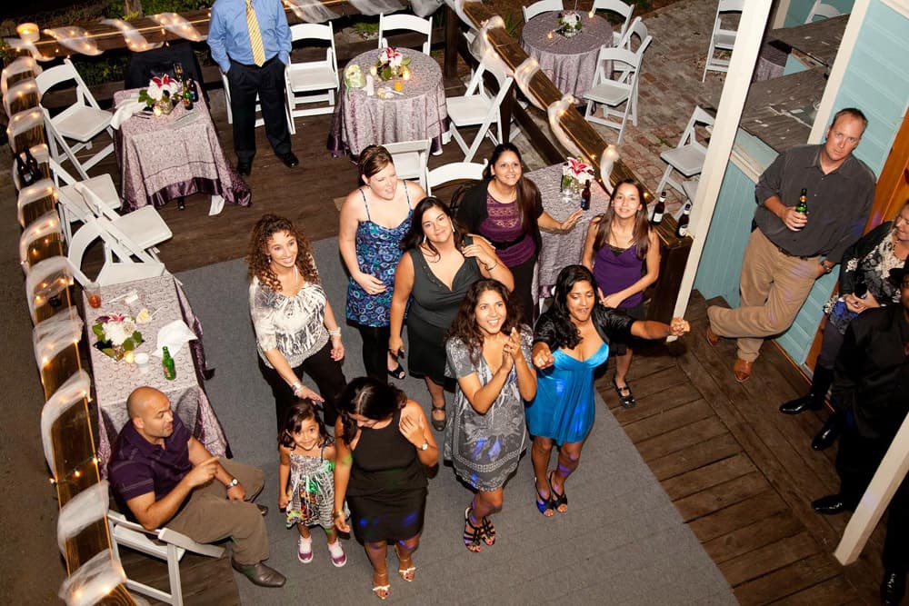 A group of people dressed in festive attire gather around decorated tables at an outdoor party.