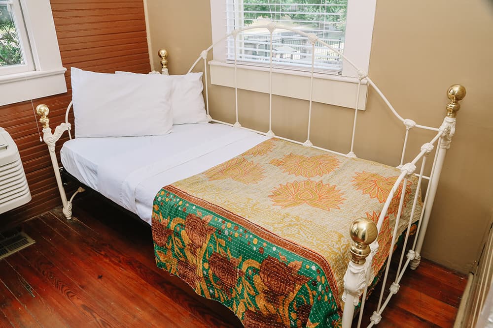 A vintage metal bed with bright pillows and a patterned quilt is positioned in a cozy room.