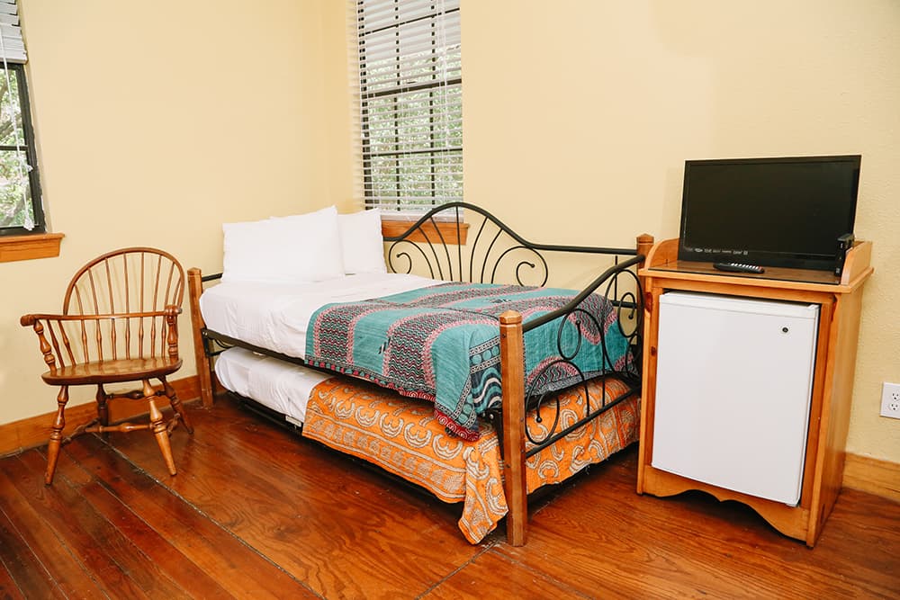 A cozy bedroom with a single bed, wooden chair, TV, and small refrigerator.