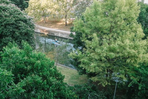 A person kayaking on a calm waterway surrounded by lush greenery.
