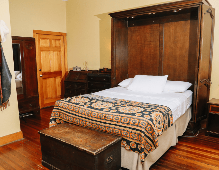 A cozy bedroom featuring a foldable wooden bed with a patterned blanket and a vintage trunk at the foot.