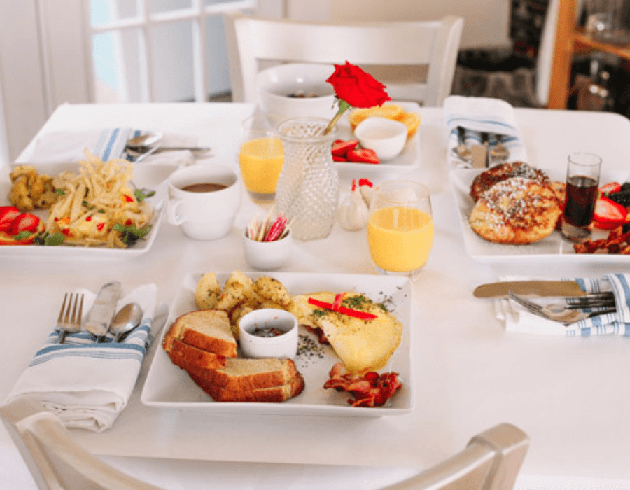 A beautifully arranged breakfast table featuring various dishes, drinks, and a vase with a rose.