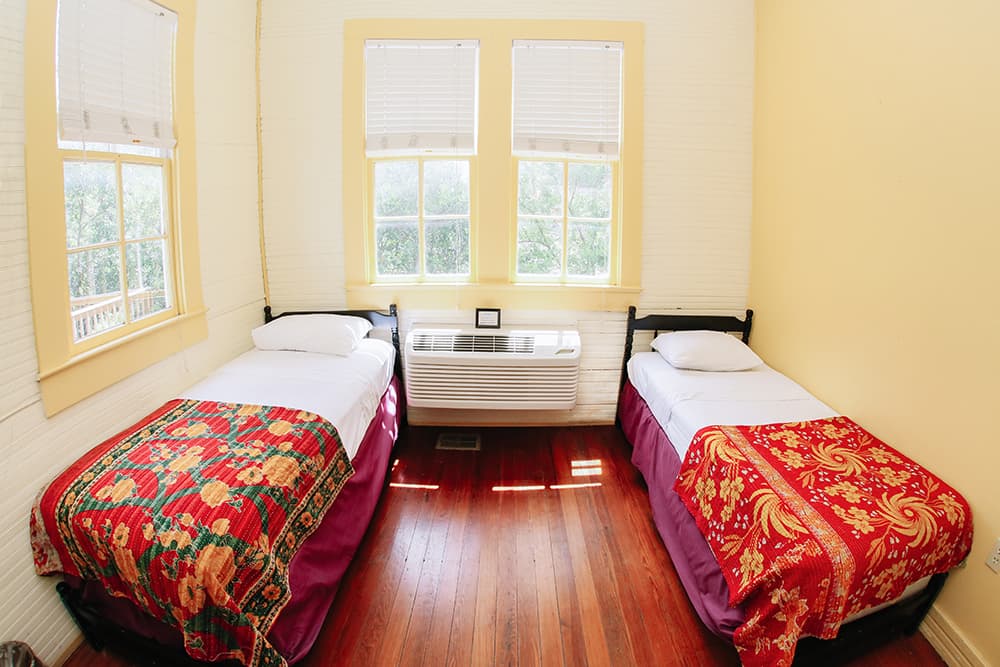 Cozy bedroom featuring two twin beds with colorful quilts and large windows.