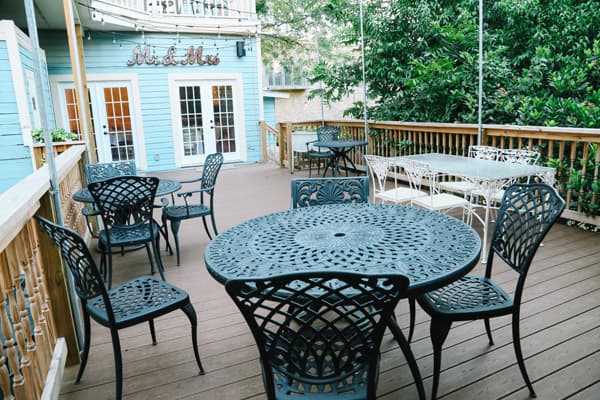 Outdoor seating area with decorative metal tables and chairs near a light blue building.