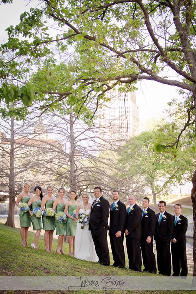 A wedding party poses outdoors, dressed in formal attire amidst blooming trees.