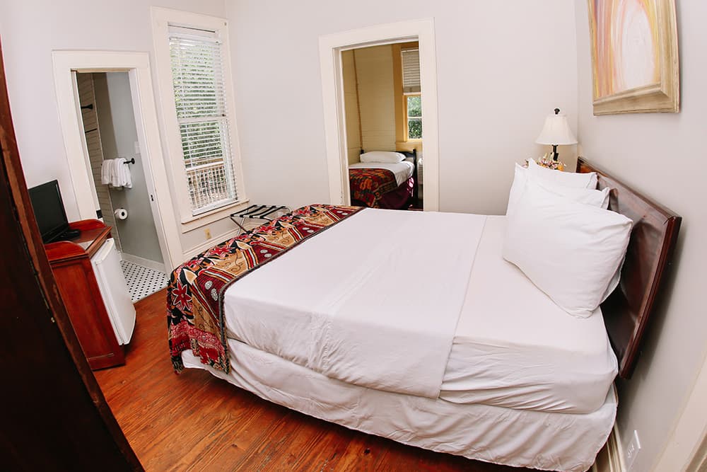 A cozy bedroom featuring a double bed with white linens and a colorful throw, with a glimpse of an adjoining bathroom.